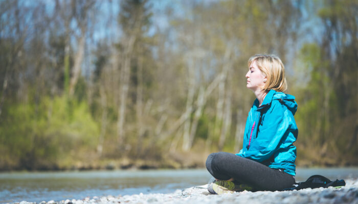 Woman is sitting on a pebble beach and doing meditation