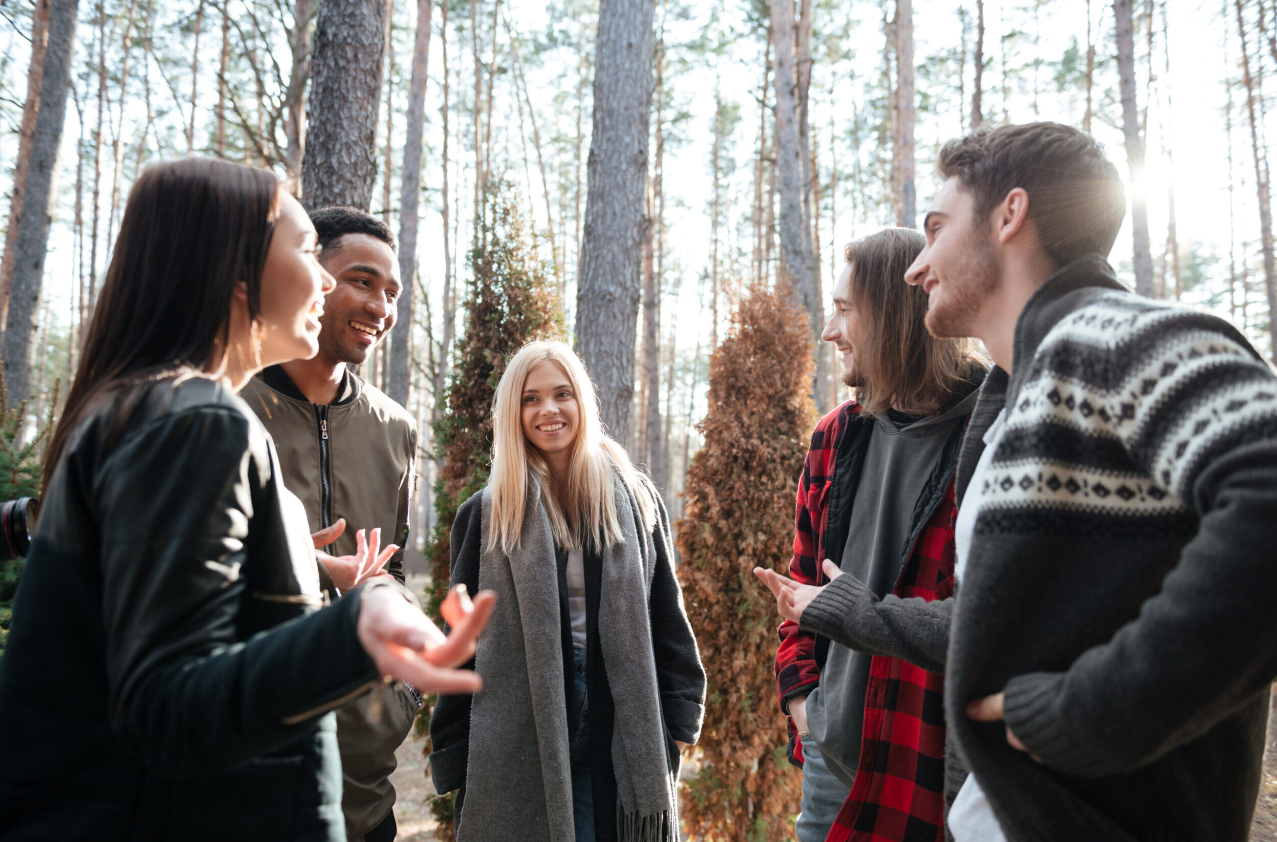 Image of happy group of friends standing outdoors in the forest looking aside and talking.