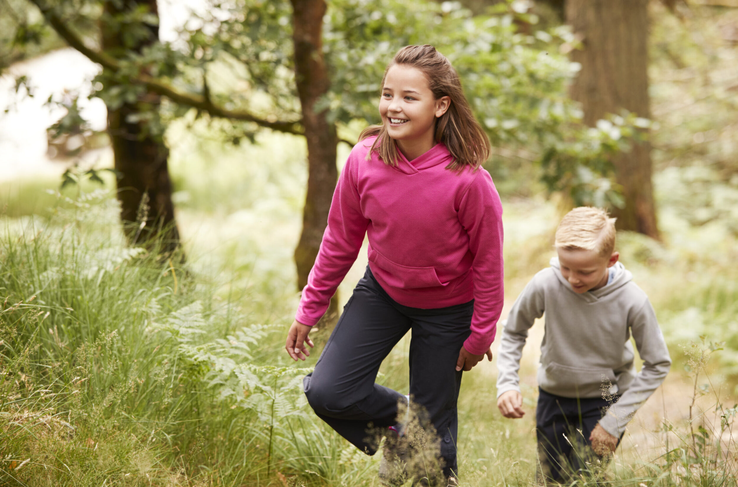 Two children walking through a forest amongst greenery, front view